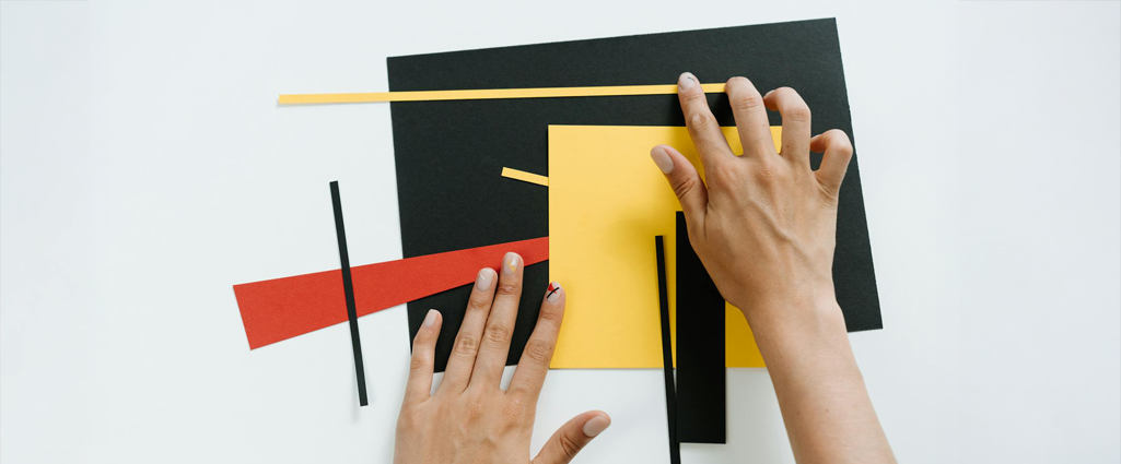 Manos creando un collage con recortes de papel de colores rojo, amarillo y negro sobre una cartulina negra